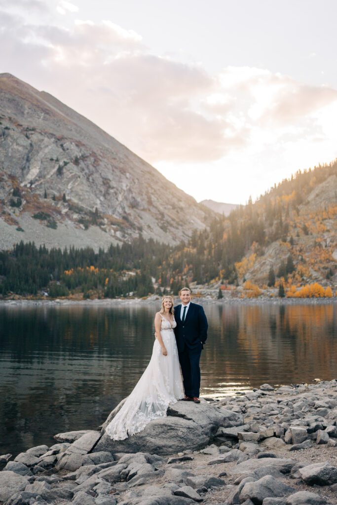 Bride and groom standing on a rock in front of an alpine lake in Breckenridge Colorado during their elopement sunset photos