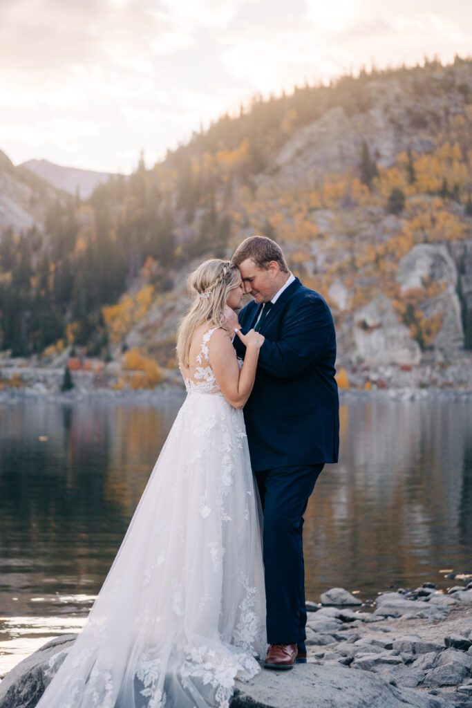 Groom holding the brides face as they touch foreheads with their eyes closed next to an alpine lake in Colorado during their Breckenridge elopement