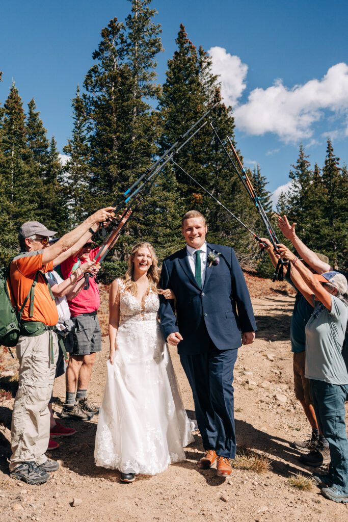 Bride and groom holding hands and walking through a tunnel of hikers holding up their trekking poles after their Breckenridge elopement ceremony