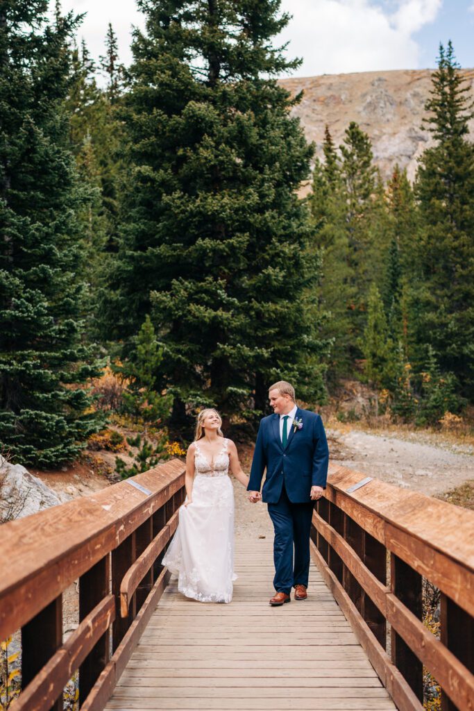 Bride and groom holding hands and walking across a bridge through the forest during their Breckenridge elopement