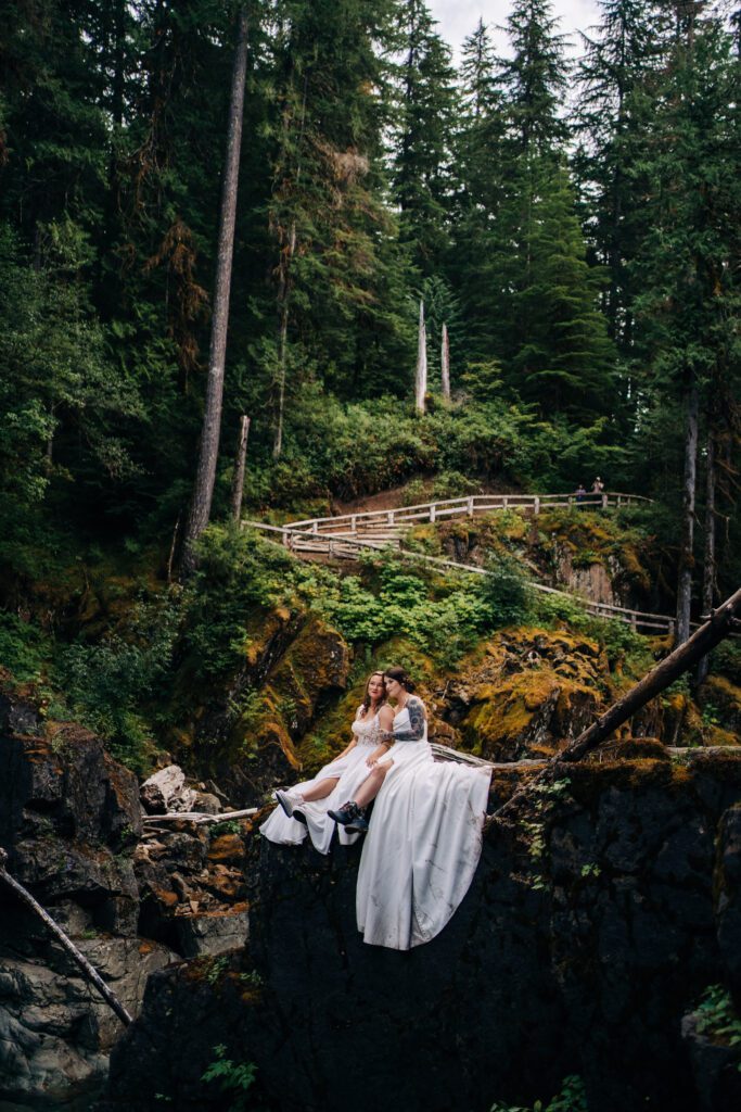 brides sitting on a cliff together after their wedding ceremony in mt rainier national park during their washington elopement