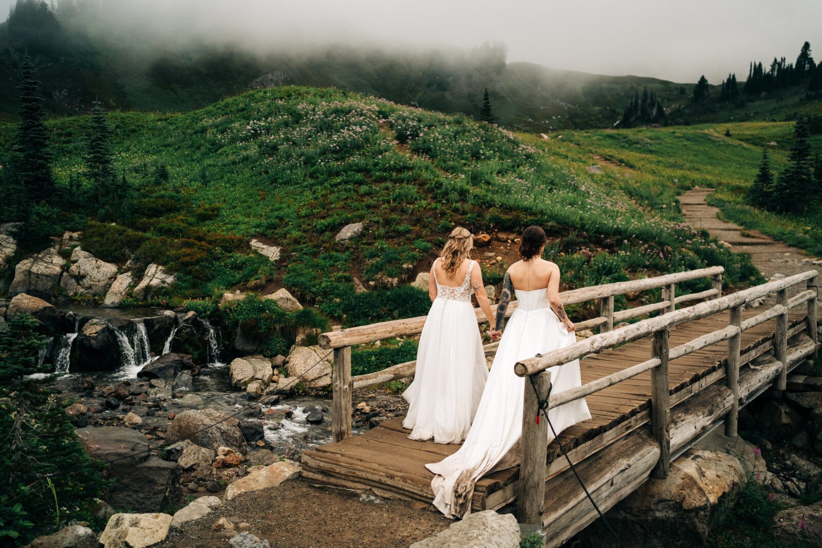 wives holding hands walking across the bridge in mt rainier national park during their washington elopement