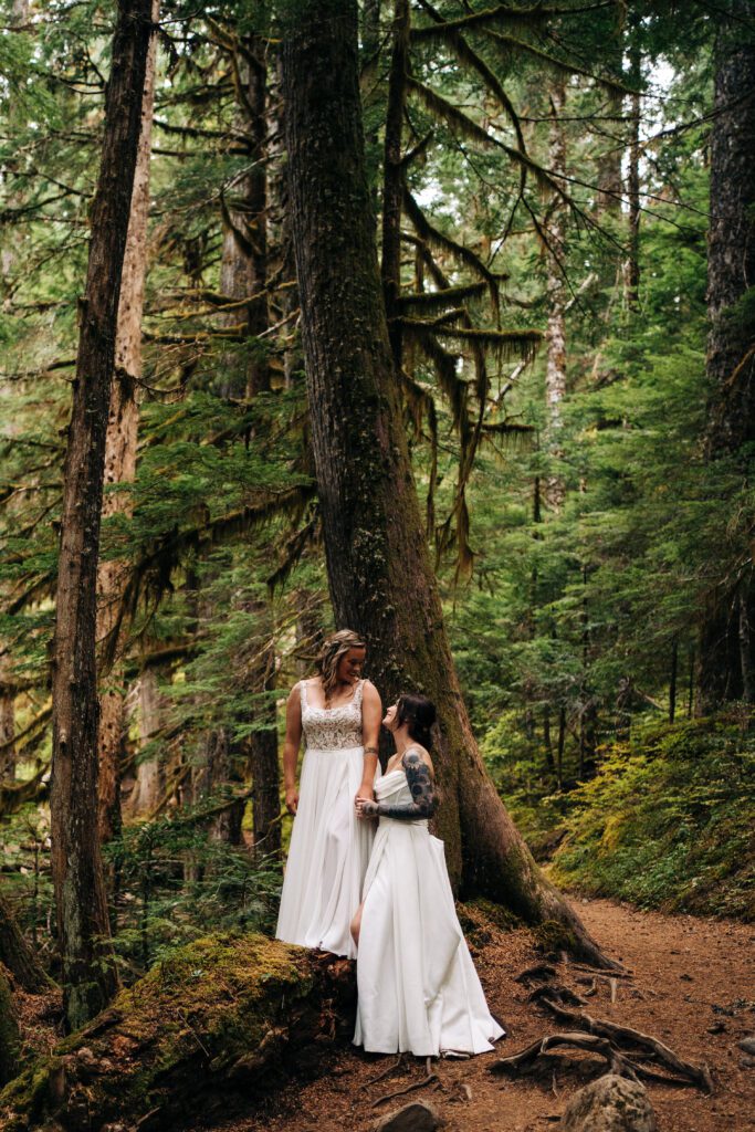 bride holding her wifes hand in the forest in mt rainier during their washington elopement