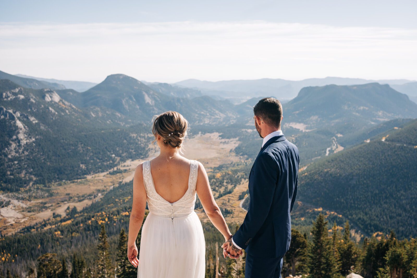 Bride and groom holding hands look out over the valley together while holding hands during their rocky mountain national park elopement