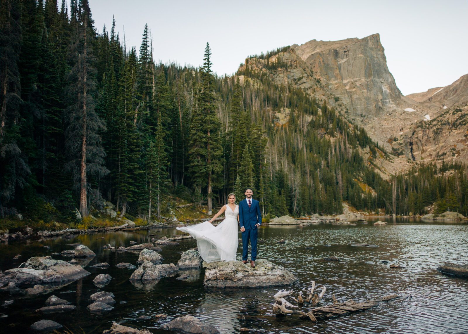 Bride and groom holding hands on a rock at Dream Lake during their Rocky Mountain National Park Elopement