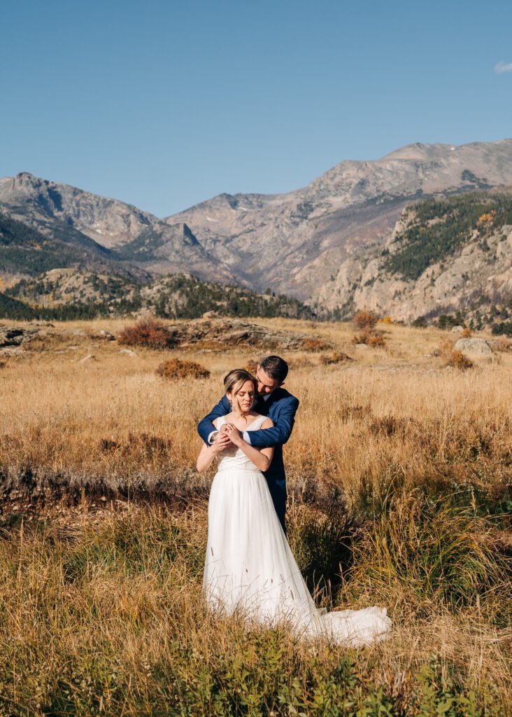 groom hugging bride from behind in Moraine Park meadows during their Rocky Mountain National Park elopement