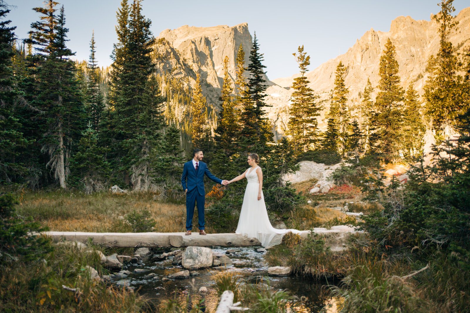 Groom holding brides hand as they cross over a bridge at Dream Lake in Rocky Mountain NP during their Rocky Mountain National Park Elopement