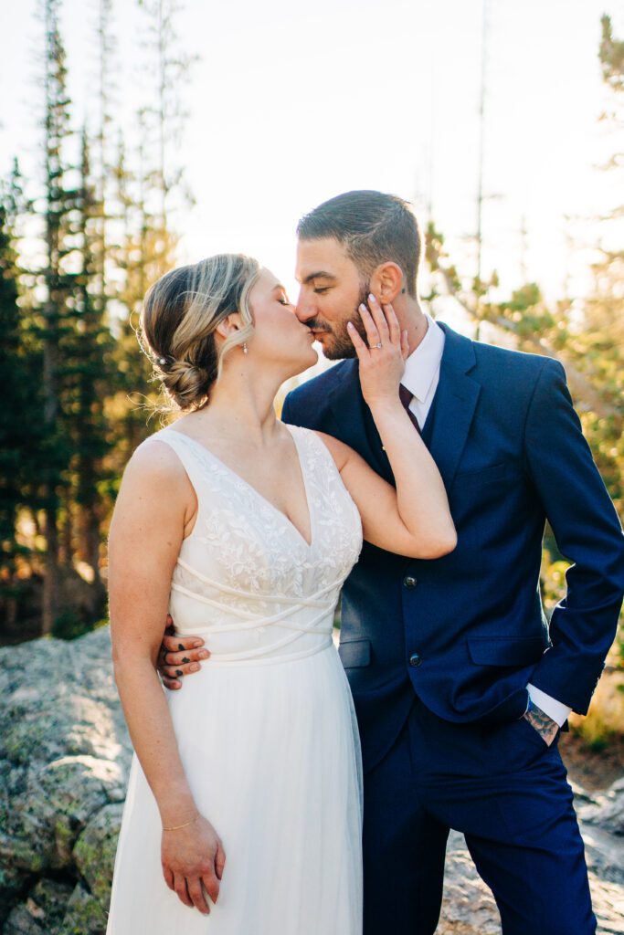 Bride reaching up to grab grooms face and kiss him during their rocky mountain national park elopement with dream lake in the background