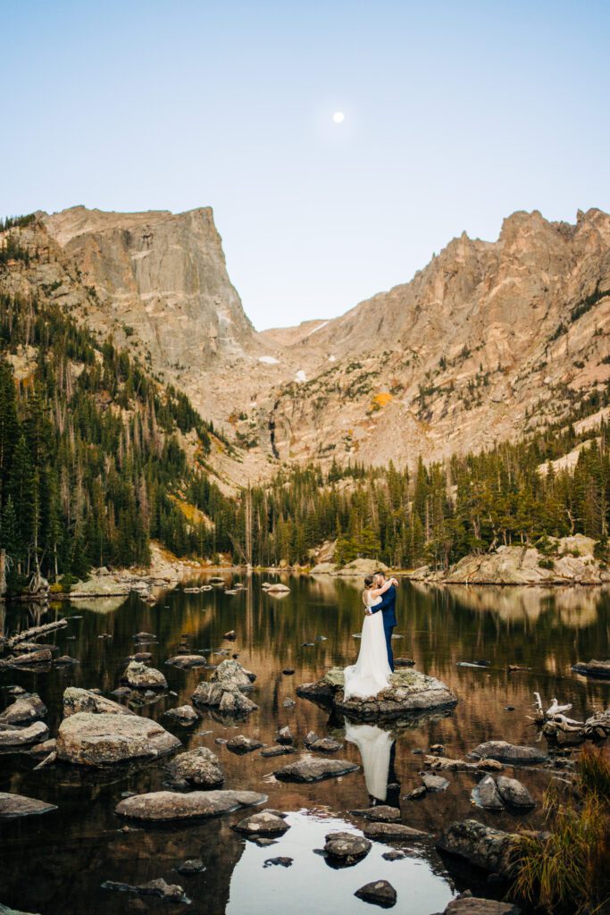 bride and groom standing on a rock in the middle of dream lake during their rocky mountain national park elopement