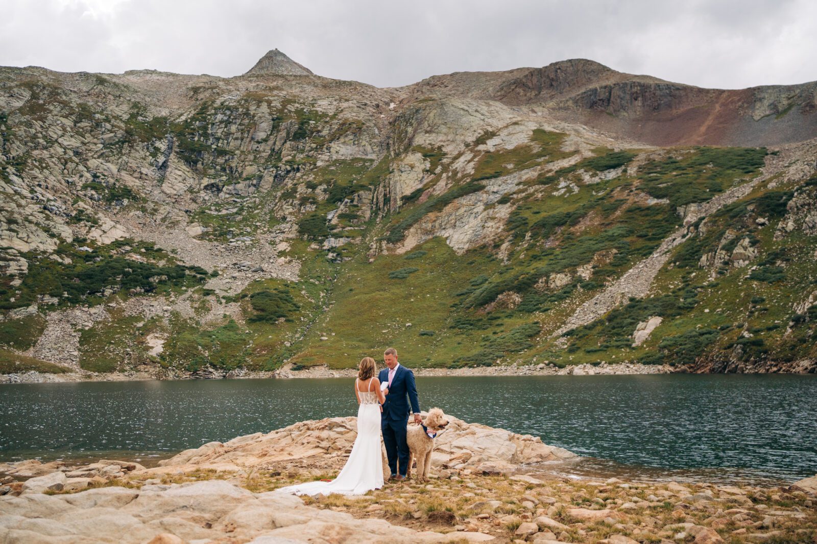 bride reading her vows to groom as they stand by the lake shore of an alpine lake during their Telluride elopement ceremony