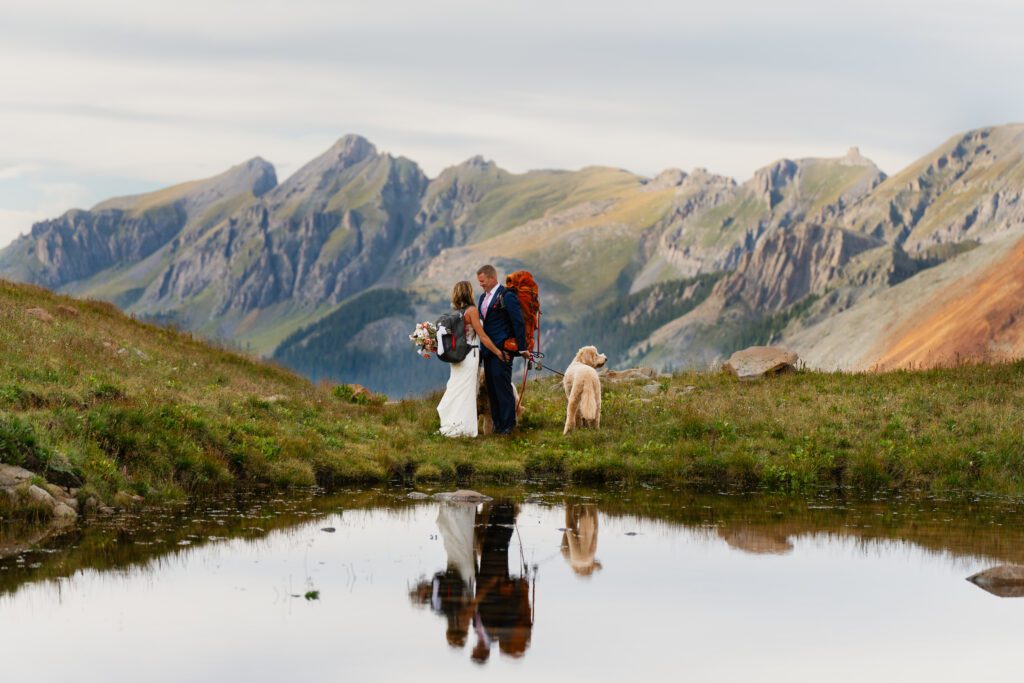 bride and groom holding hands with their hiking gear on in front of an alpine lake in the San Juan Mountains during their Telluride elopement