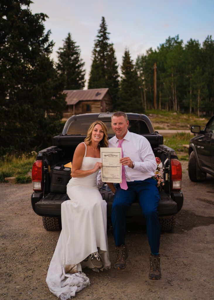 bride and groom holding their marriage license up to the camera and smiling after their Telluride elopement