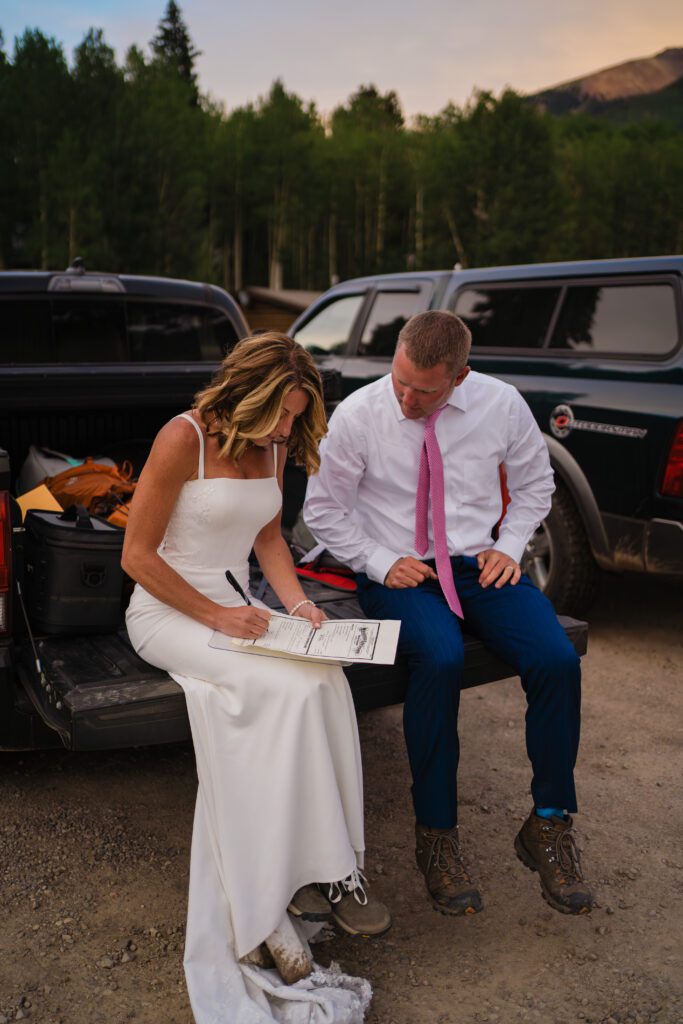 Bride signing marriage license as groom watches during their Telluride elopement