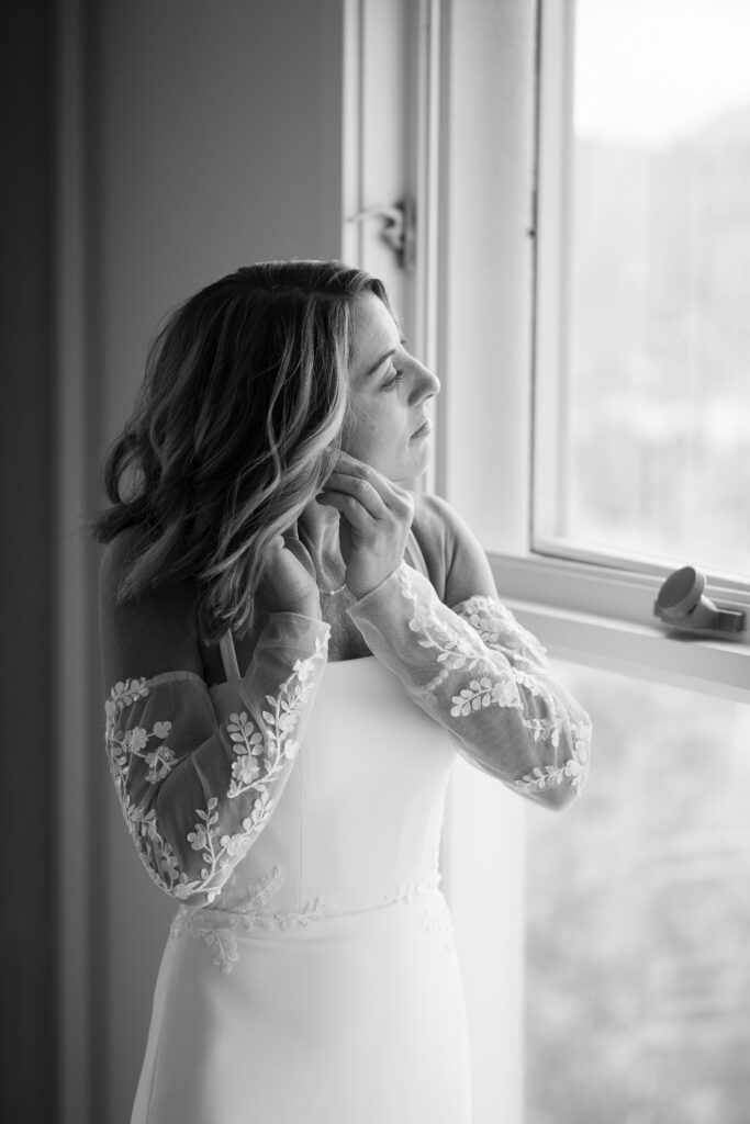 bride putting on her earrings as she looks out the window preparing for her Telluride elopement