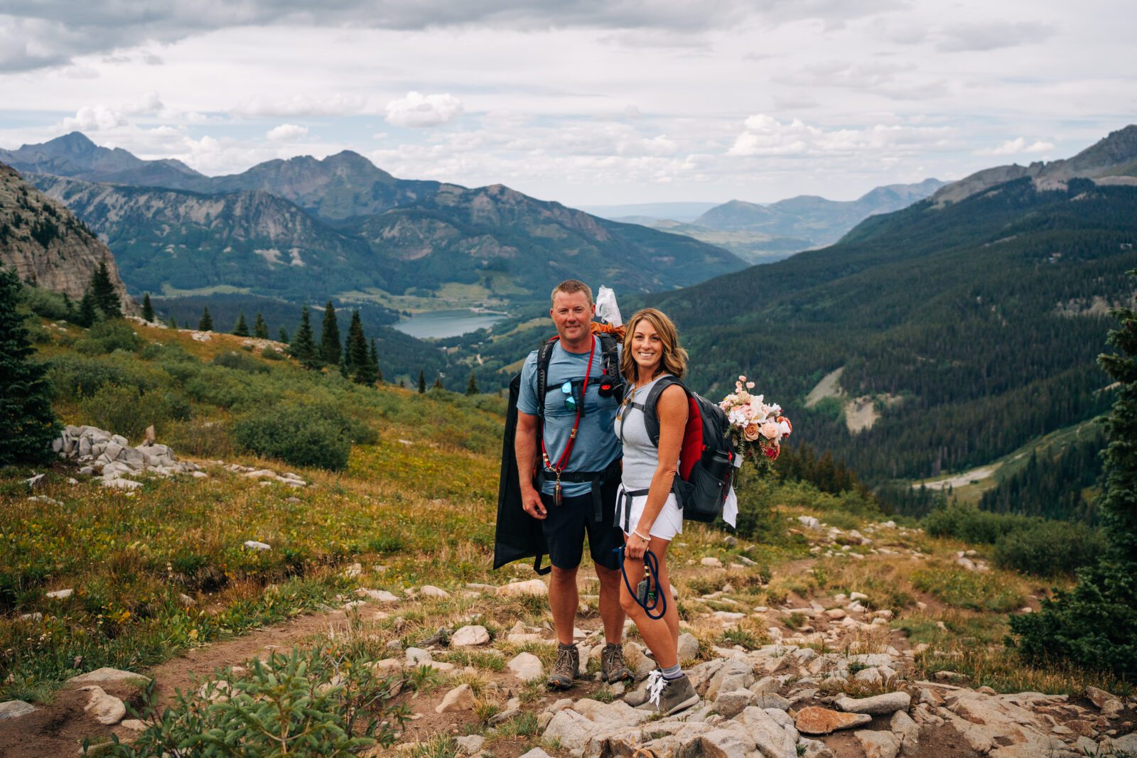 Bride and Groom smiling at the camera with sweeping mountain valleys and lakes in the background during their Telluride elopement